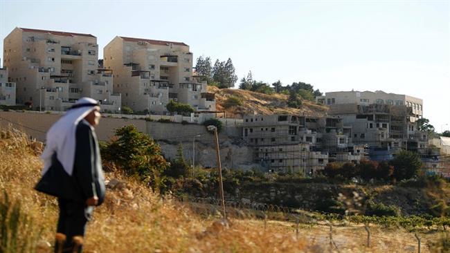 al-Khalil, also known as Hebron, on July 6, 2016, shows a Palestinian man standing in front of buildings in the illegal Kiryat Arba settlement on the outskirts of the Palestinian city. (AFP)