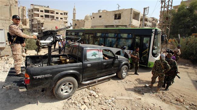 Syrian government troops stand guard as a bus carrying people drives by in the town of Daraya outside the capital, Damascus, on August 26, 2016. (Photo by AFP)