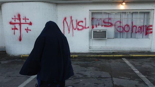 A Muslim woman seen walking past a wall spray-painted, "Muslims go home"