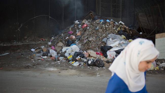 A Palestinian woman is walking past garbage along a section of the separation barrier in Shuafat refugee camp in the occupied East Jerusalem al-Quds, May 17, 2017. (Photo by AP)