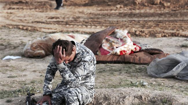 An Iraqi policeman collects himself as he is surrounded by bodies found in a mass grave in an area retaken from Daesh in Hamam al-Alil, March 15, 2017. (Photo by AP)