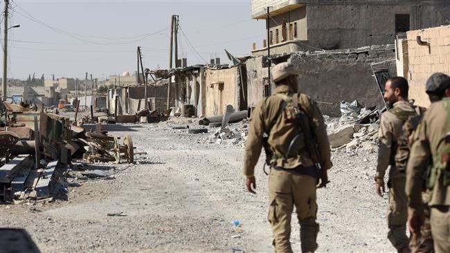 Members of the US-backed Syrian Democratic Forces (SDF) walk along a damaged street in eastern Raqqah on July 14, 2017. (AFP photo)