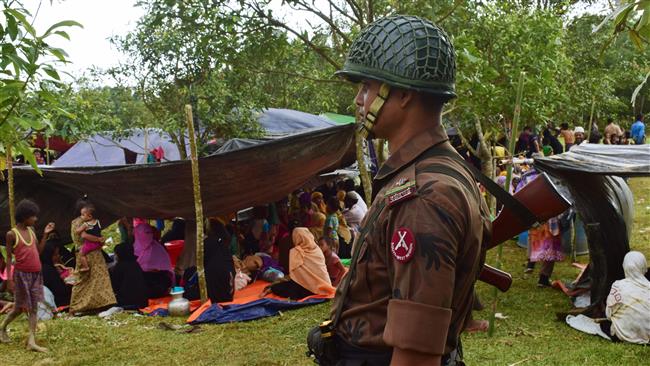 A member of the Border Guard Bangladesh personnel stands guard next to fleeing Rohingya refugees resting under a makeshift shelter, in Bangladesh, on August 27, 2017. (Photo by AFP)