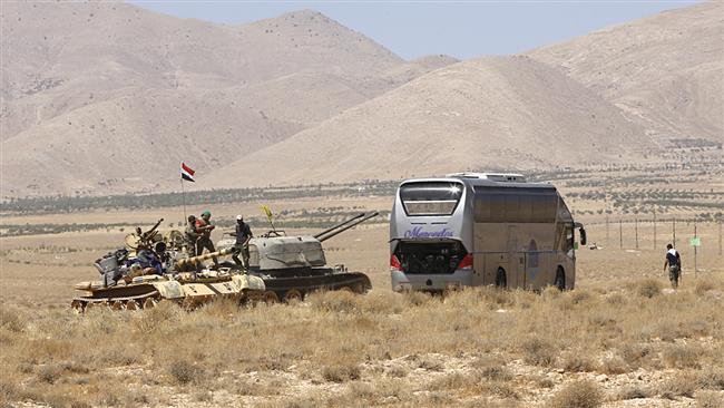 Syrian soldiers standing on a tank next to a vehicle waiting to transport the Daesh Takfiri militants are seen in the Qara area in Syria