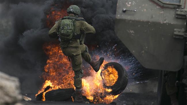 TOPSHOT - An Israeli soldier removes burning tires from the road during clashes with Palestinian protesters following a demonstration against the expropriation of Palestinian land by Israel in the village of Kfar Qaddum, near Nablus in the occupied West Bank, on September 15, 2017. (Photo by AFP)