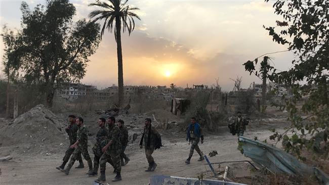 Syrian government forces walk through a road in a northeastern district of Dayr al-Zawr on November 5, 2017, after retaking the city from Takfiri Daesh terrorists. (Photo by AFP)