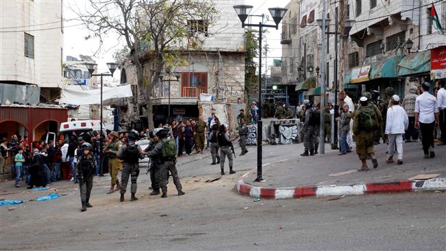 Palestinians (L) gather around an ambulance as Israeli forces (C) stand guard while Israeli settlers walk to a religious site in the city of al- Khalil Hebron in the Israeli-occupied West Bank, on November 11, 2017. (Photo by AFP)