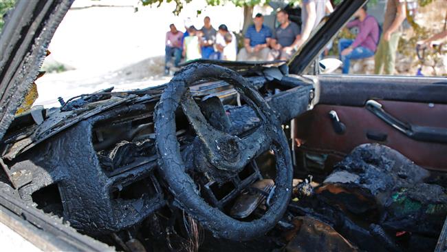Palestinians from the village of Umm Safa, west of Ramallah in the occupied West Bank, seen in the background, check a vehicle, which was set ablaze on August 9, 2017 in an apparent arson attack by Israeli settlers. (Photo by AFP)