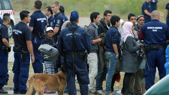 This file photo, taken on June 25, 2015, shows asylum seekers waiting to board a bus to transport them to a new refugee camp, in the Hungarian Roszke border village on Serbia’s border. (By AFP)