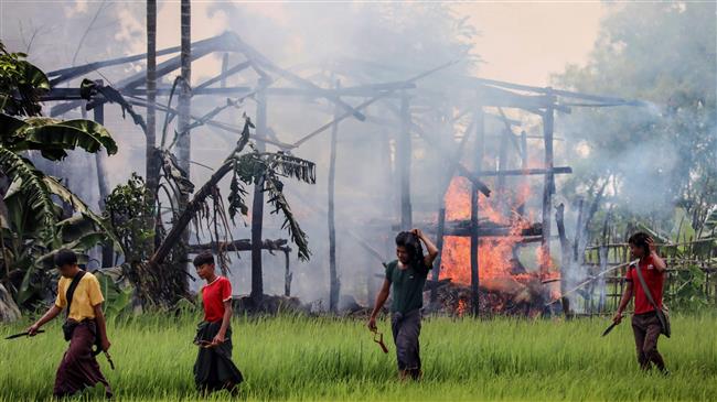 In this photo taken on September 7, 2017, unidentified men carry knives and slingshots as they walk past a burning house in Gawdu Tharya village near Maungdaw in Rakhine state in western Myanmar. (Photo by AFP)
