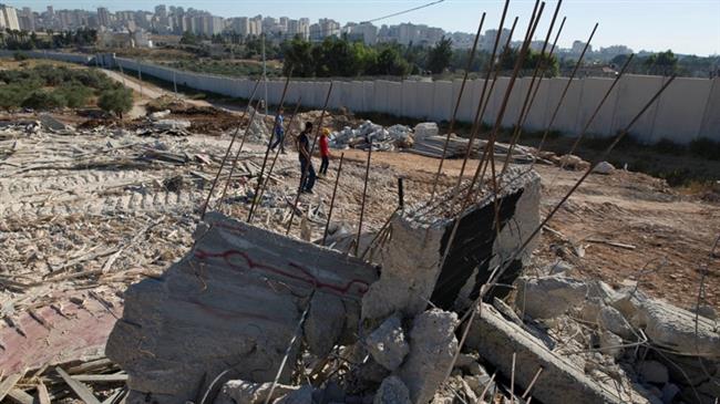 Palestinians walk over the rubble of a house that overlooks the Israeli apartheid wall, background, and was demolished by the Israeli army, in the West Bank village of Qalandia, near Ramallah, July 26, 2016. (Photo by AP)