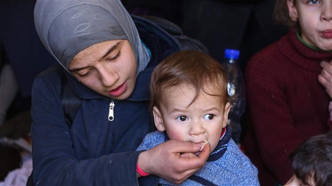 A young Syrian feeds a child while gathering with other civilians prior to evacuation to areas under government control, from the town of Jisreen in Eastern Ghouta, March 17, 2018.