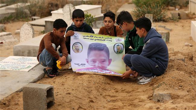 Friends of 15-year-old Palestinian victim, killed Israeli forces, hold up a poster of his portrait by his grave in a cemetery in the Gaza strip on April 21, 2018. (Photo by AFP)