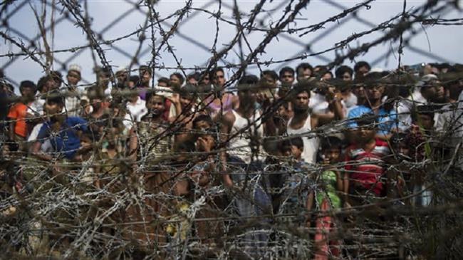 Rohingya refugees gather behind a barbed-wire fence in a temporary settlement setup in a