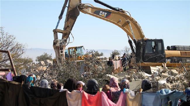 The file photo of an Israeli army bulldozer demolishing a Palestinian home in the West Bank as local women watch. (Photo by AFP)