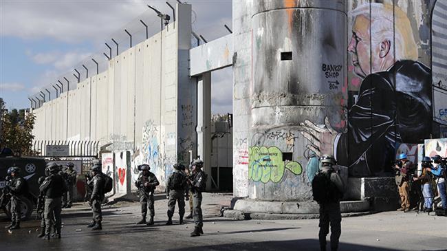 Israeli forces stand near the controversial separation wall bearing graffiti depicting US President Donald Trump during clashes with Palestinian protesters near an Israeli checkpoint in the West Bank city of Bethlehem on December 7, 2017. (Photo by AFP)