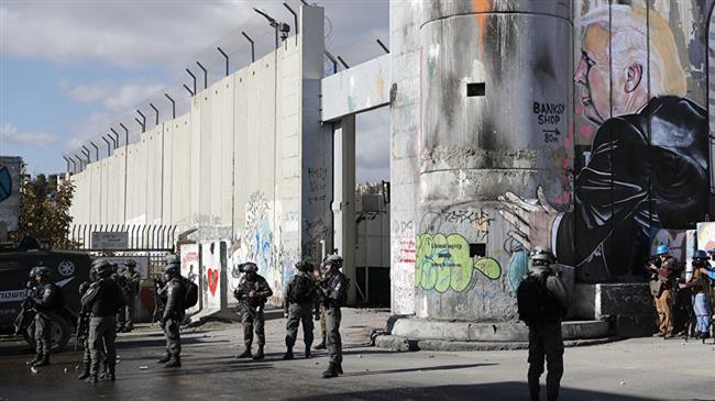 Israeli forces stand near the controversial separation wall bearing graffiti depicting US President Donald Trump during clashes with Palestinian protesters near an Israeli checkpoint in the West Bank city of Bethlehem on December 7, 2017. (Photo by AFP)