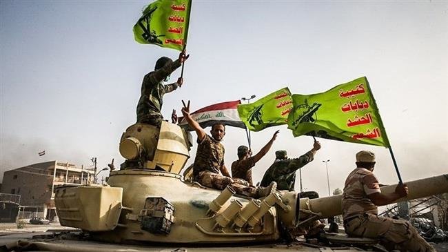 In this file picture, Iraqi pro-government fighters from Popular Mobilization Units (better known by the Arabic word Hashd al-Sha’abi) raise the national Iraqi and Popular Mobilization Forces flags as they celebrate the ouster of Daesh Takfiri terrorist group from Fallujah.