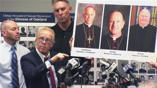 Tom Emens, right, listens as his attorney, Jeff Anderson, holds photographs of the archbishop of San Francisco and the bishops or Oakland and San Jose on Tuesday, October 23, 2018. (Photo via NBC News)