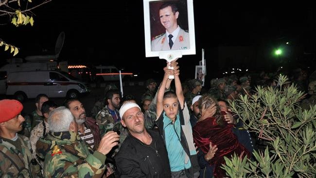 This handout picture released by SANA on November 9, 2018 shows a boy holding up a picture of Syrian President Bashar al-Assad as a group of recently-freed hostages, abducted in July from Suwayda by Daesh, are being welcomed by relatives upon their arrival overnight in their hometown in the southern Syrian province of Suwayda. (Via AFP)