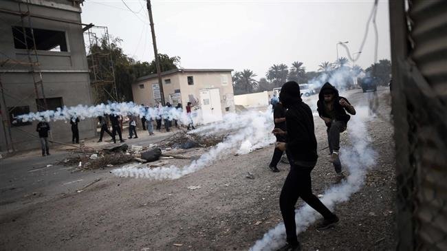 This picture, taken on February 13, 2015, shows Bahraini protesters taking cover from tear gas during clashes with police following a demonstration. (By AFP)