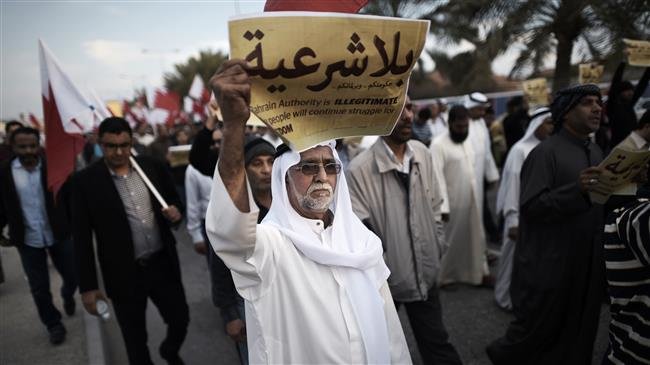 In this file photo taken on December 26, 2014, a Bahraini man holds up a placard reading in Arabic, "Your government and your parliament are without legitimacy" during an anti-government protest in the village of Jannusan, west of the capital Manama. (Photo by AFP)